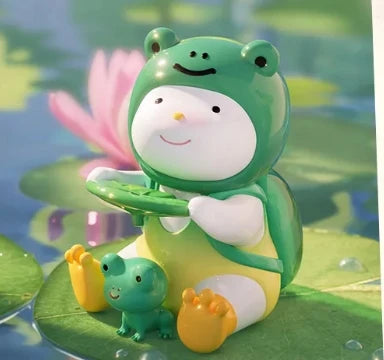 Toy frog sitting on a lily pad with a smaller frog figure beside it, against a pond background.
