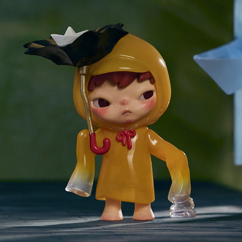 Toy figure in a yellow raincoat with an umbrella against a blurred green background