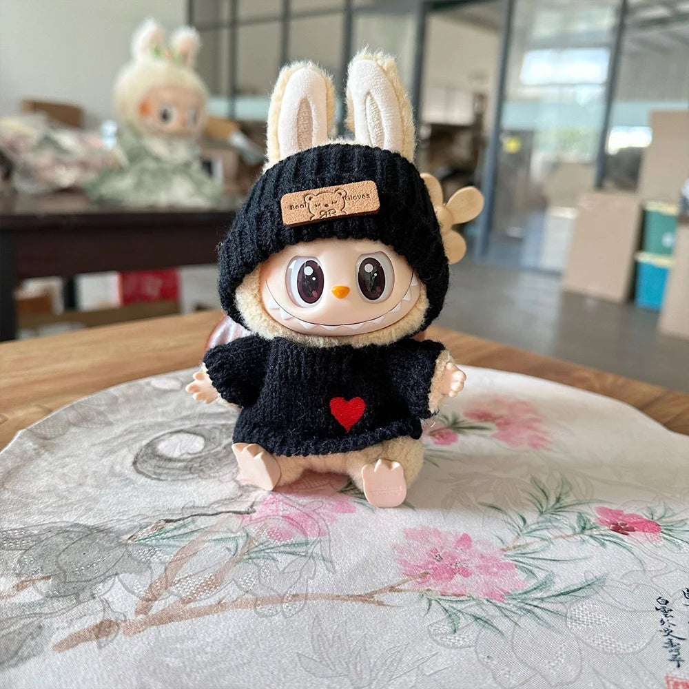 Toy figure wearing a black knitted hat and sweater with a heart on a floral-patterned surface.