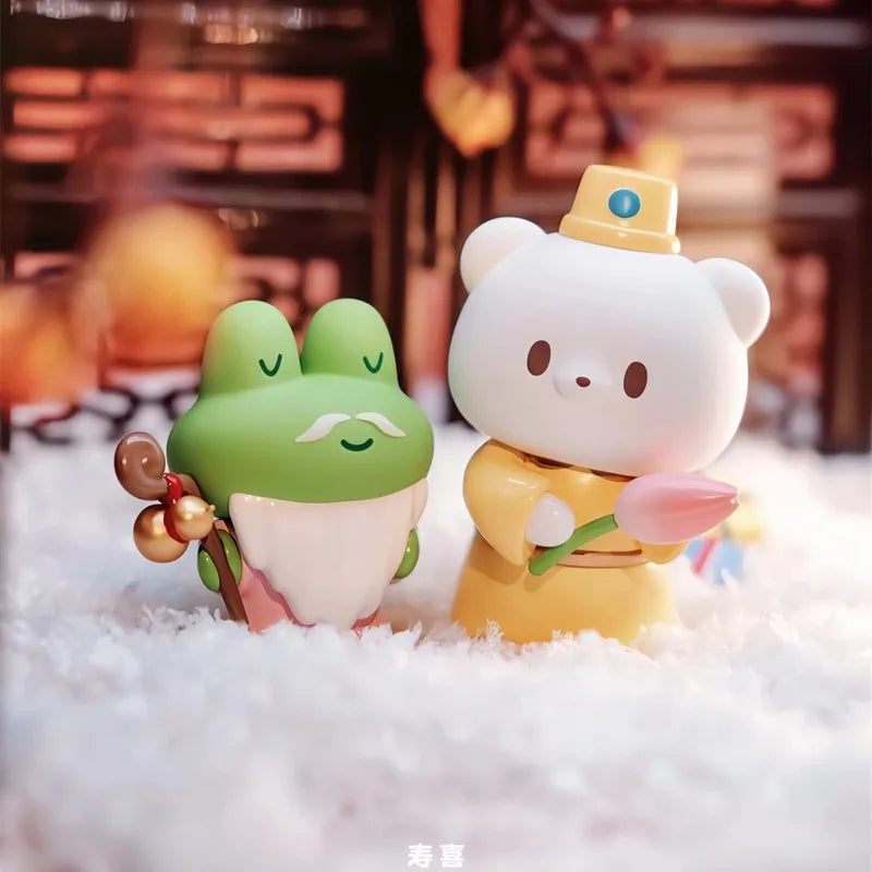 Two cartoon-style figurines, one green and one yellow, sitting on a fluffy white surface with a blurred background.