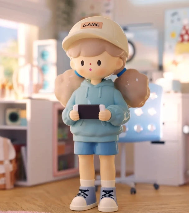 Toy figure of a character wearing a cap and holding a game controller in a room setting.