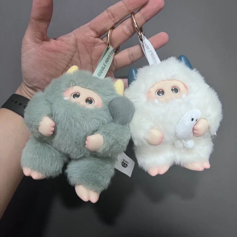 Two fluffy keychains, one gray and one white, held in a hand against a dark background.