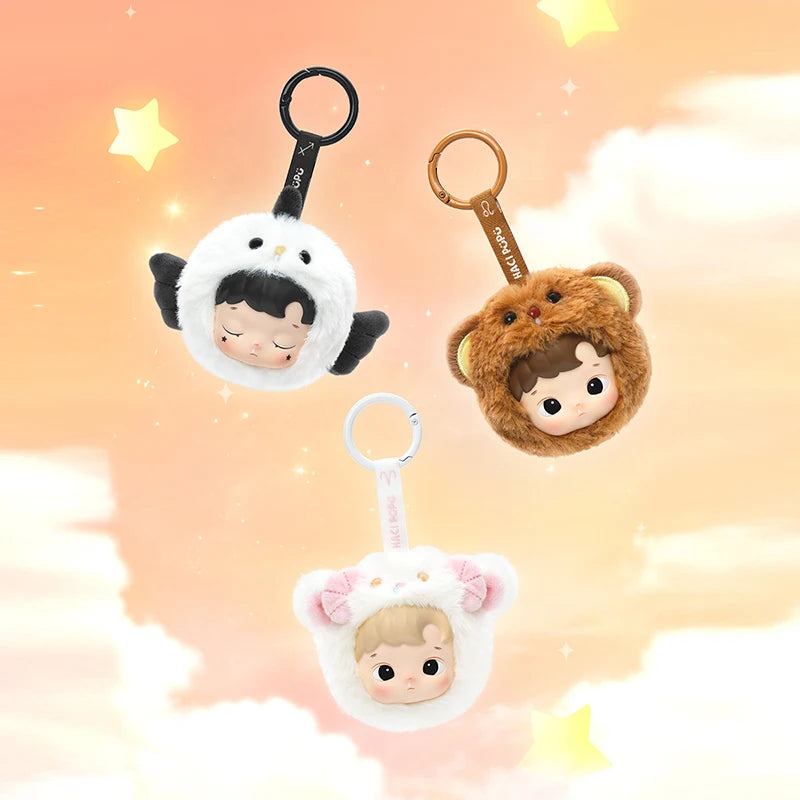 Three plush keychains with cartoon character faces on a soft, gradient background.