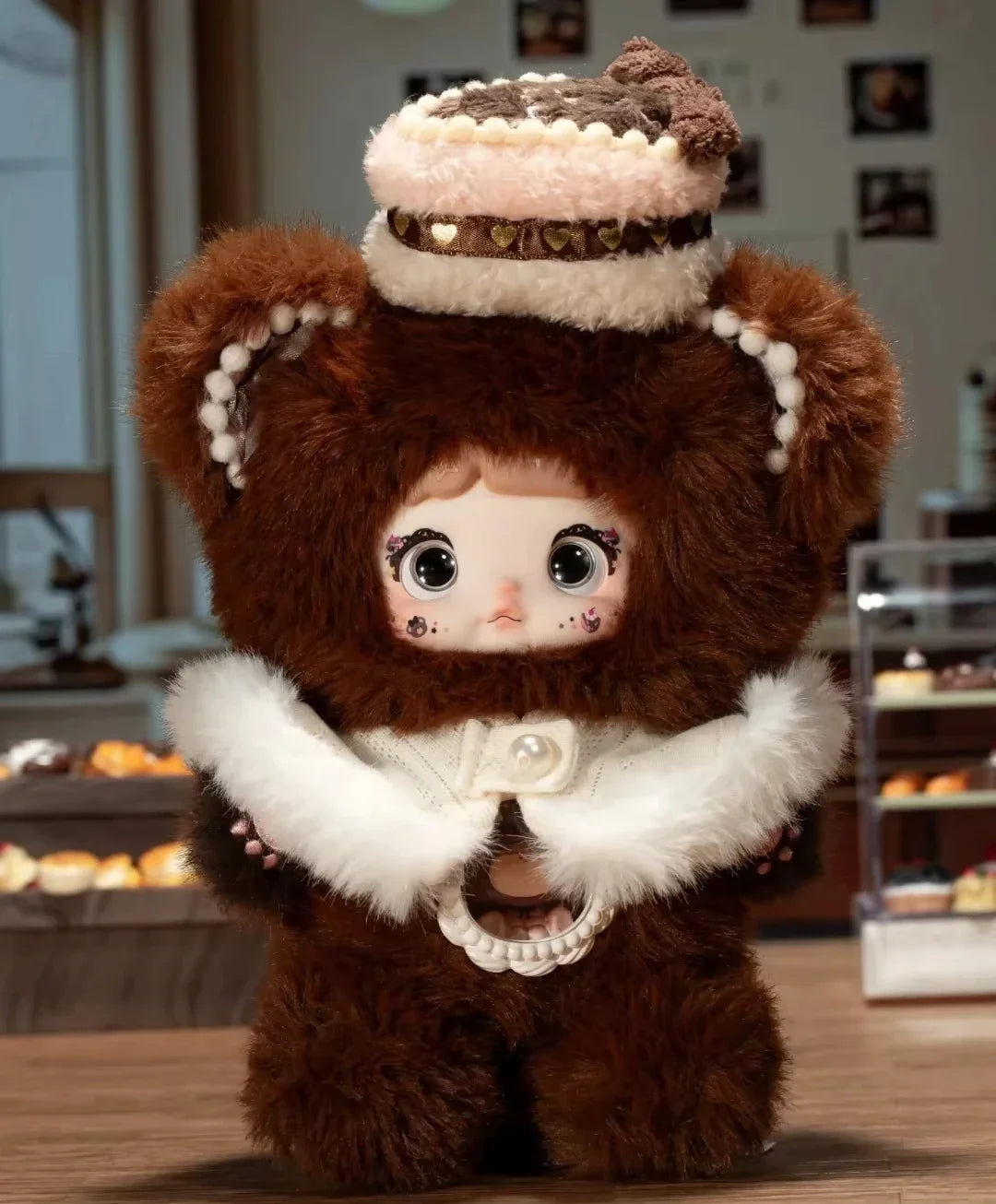 Plush toy with brown fur, white accents, and a crown-like headpiece in a blurred indoor setting.