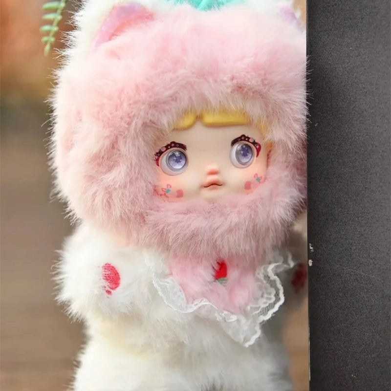 Toy figure with pink fur hood and white outfit peeking from behind a black object
