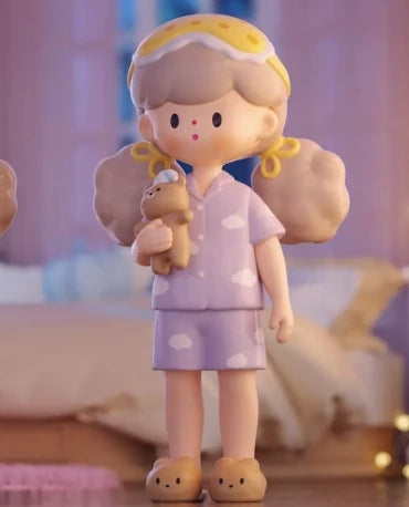 Toy figure of a girl in pajamas holding a teddy bear in a bedroom setting