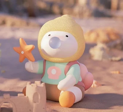 Toy figure with a yellow hood and colorful outfit sitting on sand with a starfish