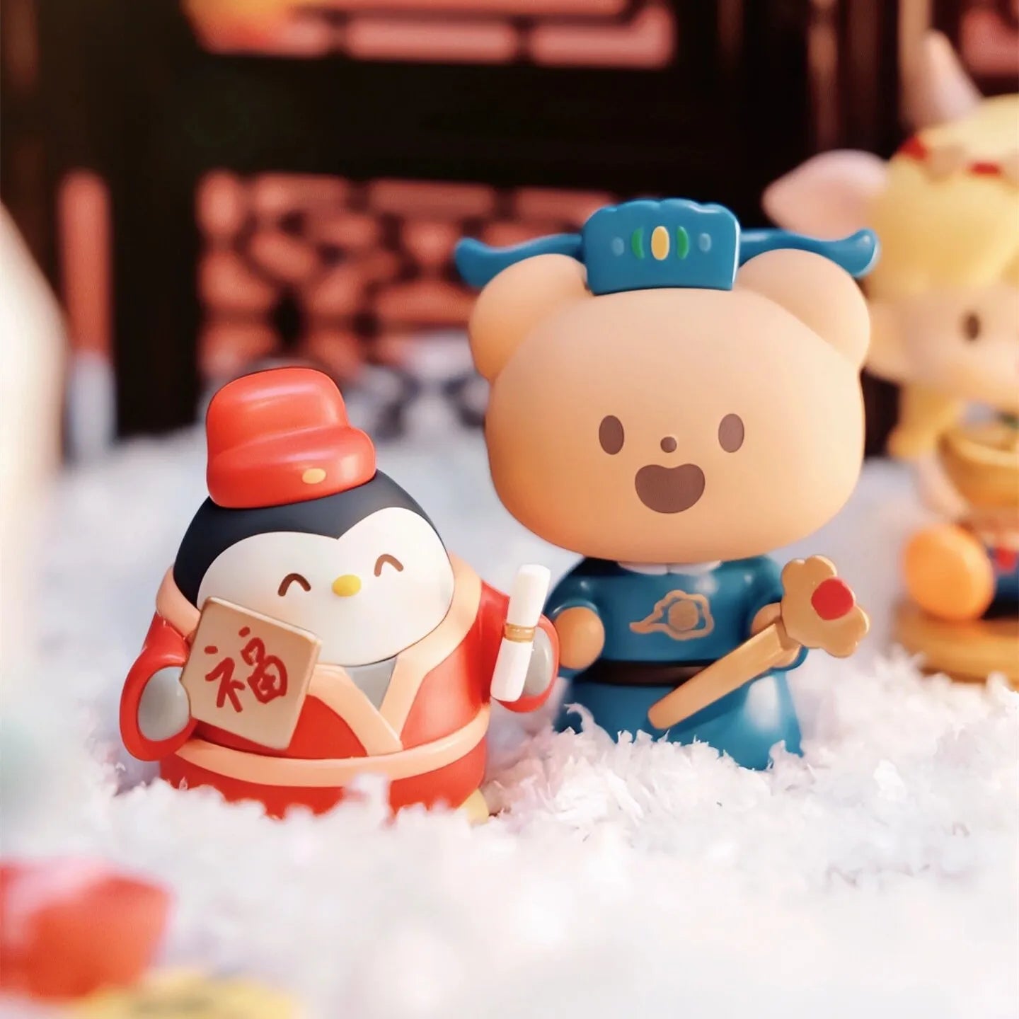 Two cartoon figurines, one penguin and one bear, standing on a snowy surface with a blurred background.