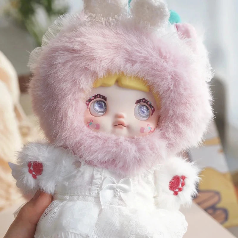 Toy figure with pink fluffy hood and white outfit held by a hand