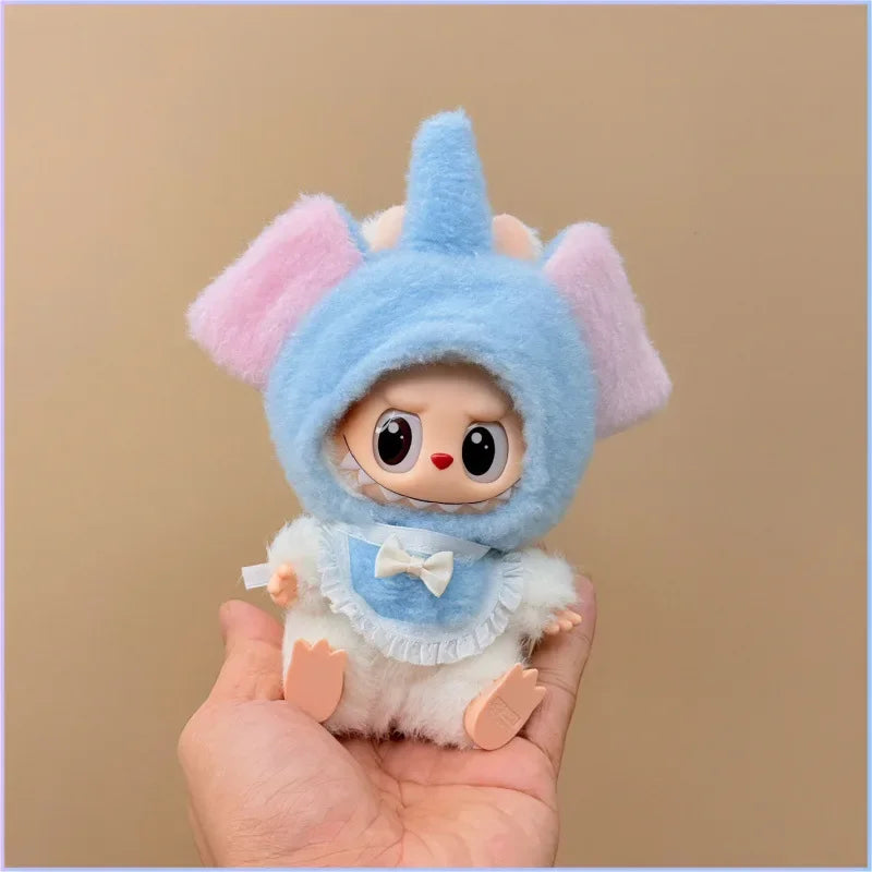 Small plush toy with a blue hood and pink ears held in a hand against a beige background