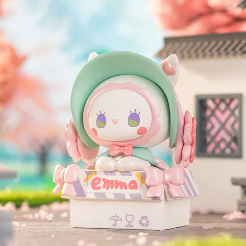 Cute figurine with a green hat and pink bow, standing on a stand with 'Emma' written on it, against a blurred background.