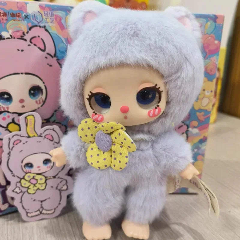 Plush toy with a gray hood and yellow bow in front of colorful packaging