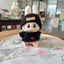 Toy figure wearing a black knitted hat and sweater with a heart on a floral-patterned surface.