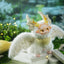 Fantasy creature with white fur, yellow accents, and antlers standing on a platform with a blurred natural background.