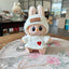 Toy figure with bunny ears and a white sweater with a red heart on a floral tablecloth.