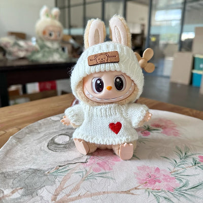 Toy figure with bunny ears and a white sweater with a red heart on a floral tablecloth.