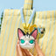 Cat-shaped keychain held by a hand with a striped yellow bag in the background