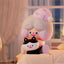 Cute character with pink hair and a black and white cat plush toy on a bed.
