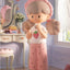 Toy figure of a girl with a strawberry shirt and pink skirt in a room setting.