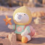 Toy figure with a yellow hood and colorful outfit sitting on sand with a starfish