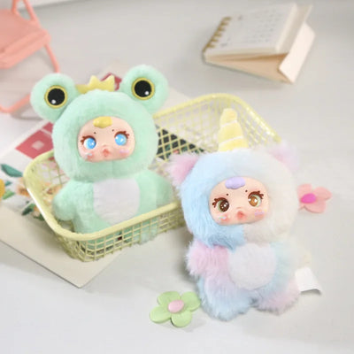 Two colorful plush toys, one green and one multicolored, on a light surface with a basket and book in the background.