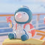 Cartoon character with a blue helmet and pink cheeks sitting on a yellow surface with a blurred background