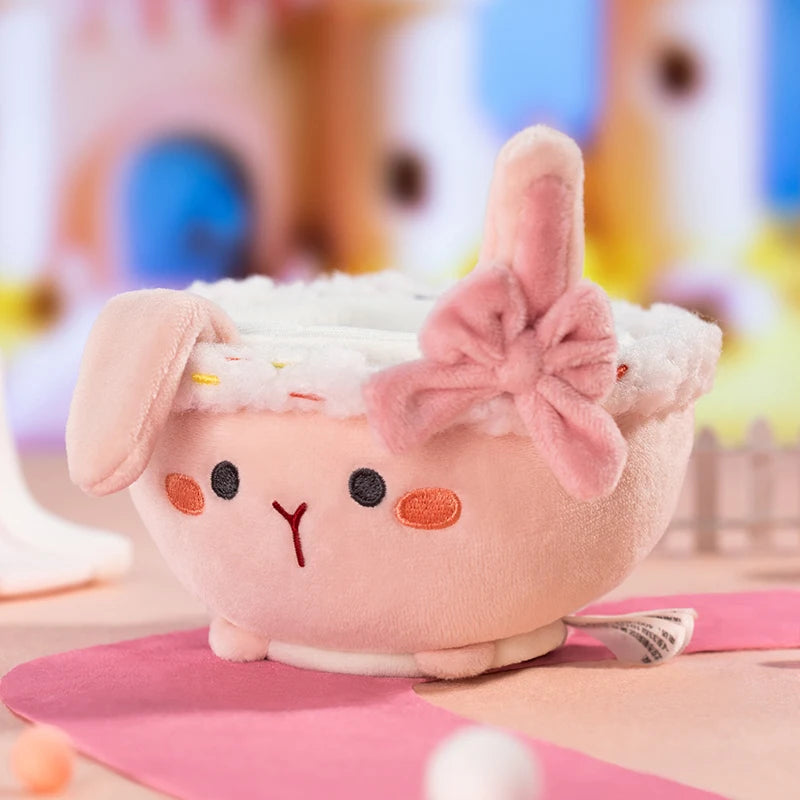 Plush toy resembling a cupcake with rabbit ears and a bow on a colorful background