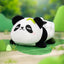 Plush panda toy sitting on a green surface with a blurred natural background