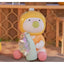 Toy figure with a yellow head, orange body, and pink legs holding a green object on a wooden surface.