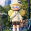 Toy figure of a person wearing a helmet and sunglasses, standing in a park-like setting with a bicycle and bench in the background.