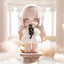 Cute character with pink hair and large eyes holding a black plush toy in an elegant indoor setting.